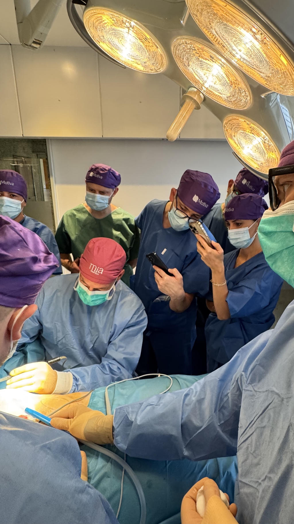 Skupina kirurgov v operacijski dvorani izvaja poseg na prsnem delu pacienta pod močno operacijsko svetilko.