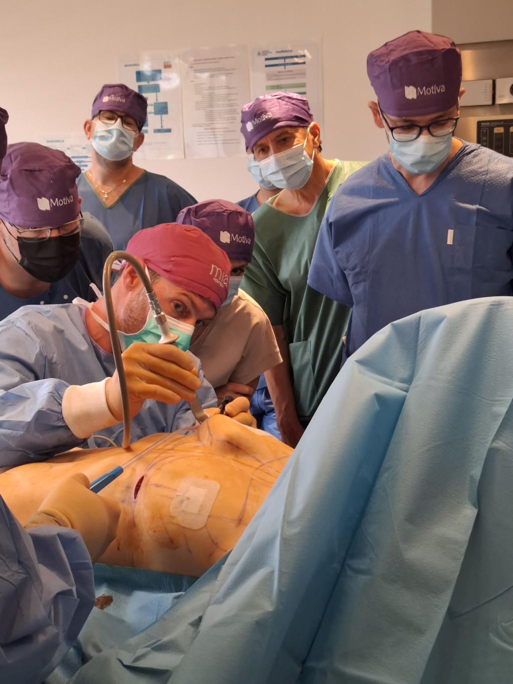 Kirurška ekipa med natančnim postopkom na pacientu, obkrožena s strokovnjaki, ki opazujejo in dokumentirajo postopek.