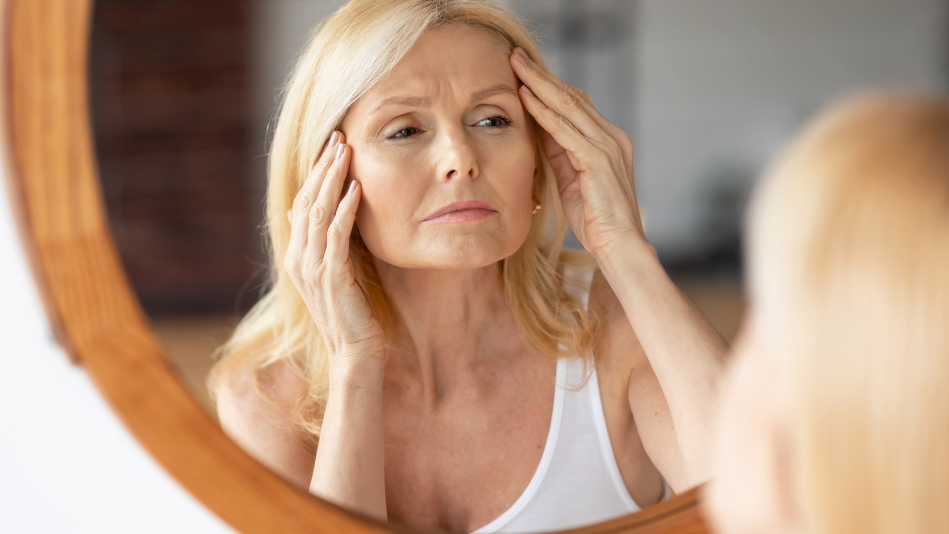 Ženska pred ogledalom, opazuje prve znake staranja in razmišja o faceliftu